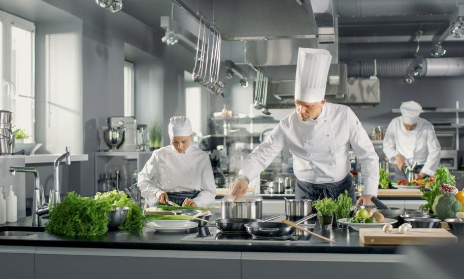 Mehrere Köche arbeiten in einer Großküche und bereiten Gerichte zu